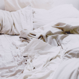 An untidy bed with white sheets and pillows.