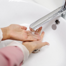 Close up of a woman's arms, washing her hands in a sink.