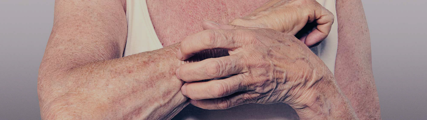 A close up of a man's upper torso wearing a vest, his left hand is is itching his right forearm